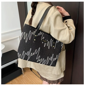 Macro detail of black quilted tote bag with white wave stitching and gold logo plaque