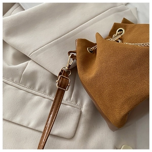 Detail of a brown frosted suede bucket bag with gold chain drawstring and fine stitching