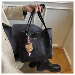 Close-up of black matte leather tote bag with woven handles and cute plush bear charm