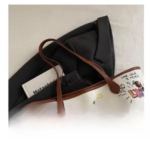 Detail of white graffiti tote bag featuring brown leather handles and gold metal hardware