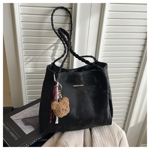 Detail of black tote bag with braided handles and a brown plush bear charm accessory