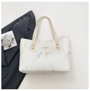 Detailed view of white textured tote bag with colorful embroidery and gold rivet accents