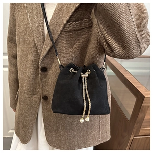 Detail of black suede drawstring bucket bag with gold chain and pearl embellishments