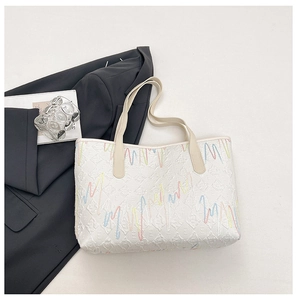 Detail of white tote bag featuring colorful zigzag embroidery and monogram textures