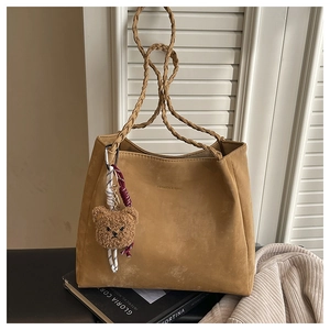 Detail of a large brown tote bag with braided handles and a plush bear pendant charm