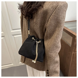 Detail of black bucket bag with gold chain drawstring and pearl charms on a model