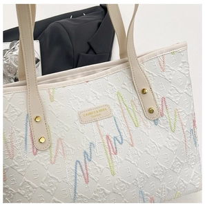 Detail of off-white tote bag showing embossed texture, wavy embroidery, and logo plaque