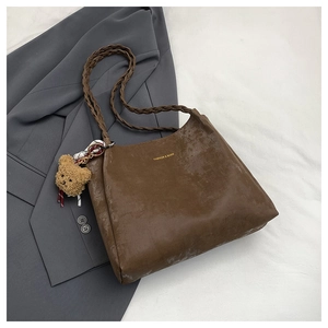 Detail of vintage brown tote bag featuring woven handle, plush bear charm and fashion text