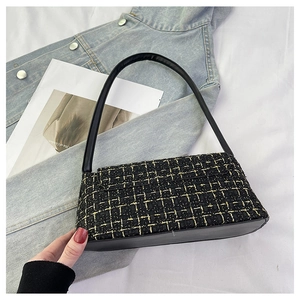 Dettaglio della trama in tweed nero e oro su questa elegante borsa baguette in pelle