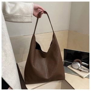 Détail d'un cabas tressé marron foncé avec de longues anses dans un décor de bureau épuré