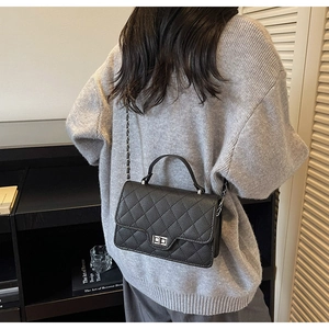 Detail of black quilted chain bag with silver twist lock on a grey sweater backdrop