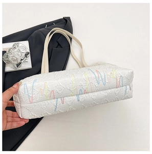 Detail of white tote bag with textured surface and colorful wavy embroidery accents