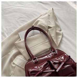 Detail view of burgundy faux leather bag featuring chic bow-decorated front flap pockets