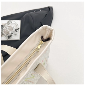 Detail of cream tote bag featuring intricate floral lace embroidery and gold metal zipper