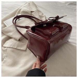 Detail of dark red glossy faux leather shoulder bag featuring bow decor and double pockets