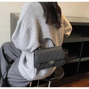 Rear view of a model wearing a black quilted leather crossbody bag with silver chain strap