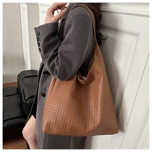 Sac fourre-tout en cuir tressé caramel avec large bandoulière porté par un mannequin