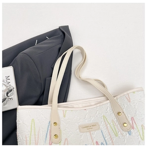 Detail of white quilted tote bag featuring colorful embroidery and logo plaque