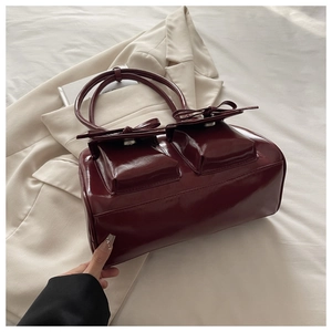 Detail of burgundy glossy leather handbag featuring front double pockets and chic bows
