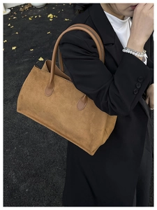 Close-up of brown suede tote bag carried by model over a black blazer for autumn