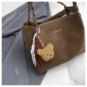 Detail of dark brown suede tote bag with woven handles and cute bear charm accessory