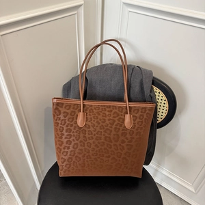 Fashionable leopard print tote bag with brown leather straps on a stylish black chair