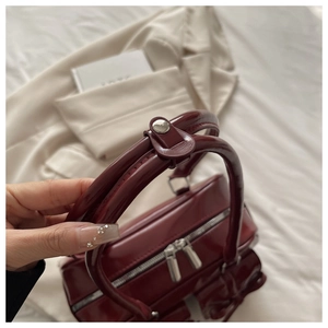 Detail of burgundy patent leather bag with double zippers and metallic luster