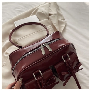 Close-up of deep red glossy shoulder bag with bow details and silver dual zippers