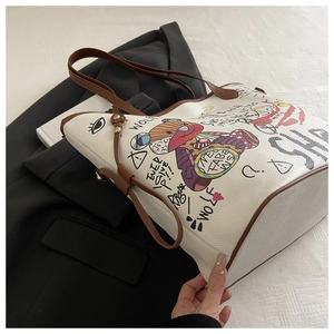 Close-up of white tote bag featuring artistic graffiti patterns and brown leather handles