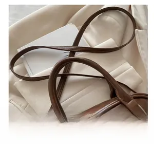 Detail view of smooth leather handle and silver metal hardware on brown crossbody bag