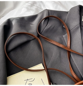 Détail de la fine bandoulière en cuir marron avec coutures précises sur un costume gris