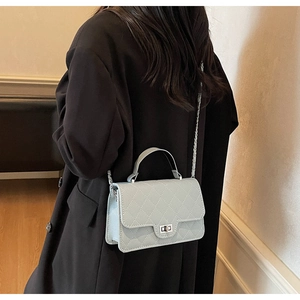 Close-up of mint blue quilted crossbody bag with silver chain strap on a black coat