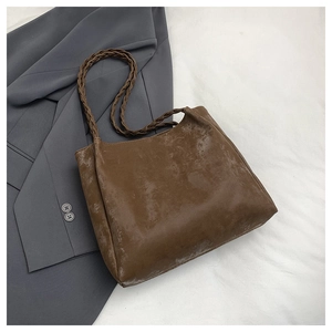 Detail of vintage brown tote bag featuring braided handles and textured faux leather surface