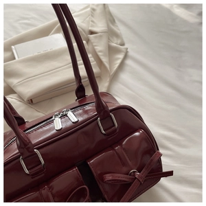 Detail of dark wine red patent leather shoulder bag with decorative bows and twin front pockets