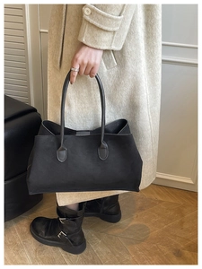 Detail of a black suede tote bag being carried by a model in a beige cashmere coat