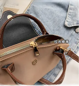 Close-up of golden zipper and leather trim on beige canvas crossbody handbag detail