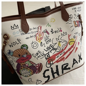 Close-up of white pebble leather tote bag with colorful graffiti and bear patches