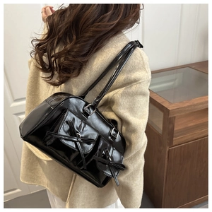 Glossy black patent leather shoulder bag with vintage bow details worn by a model