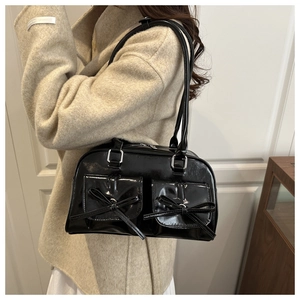 Close-up of a glossy black shoulder bag featuring bow details on a wool coat model