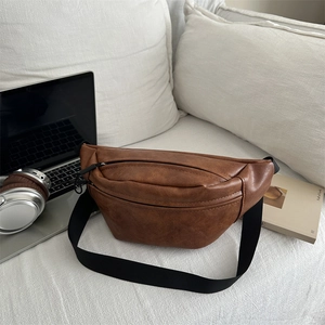 Brown vintage textured leather chest bag with adjustable strap on white sofa