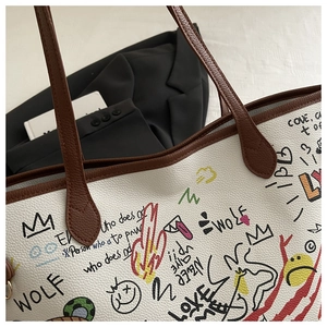 Detail of white litchi pattern tote bag with creative graffiti and brown leather strap