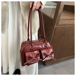 Detail of dark red patent leather shoulder bag with chic bow accents and dual front pockets