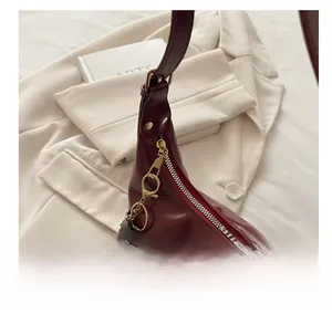 Detail showing the smooth golden metal zipper and dark red leather of the crescent bag