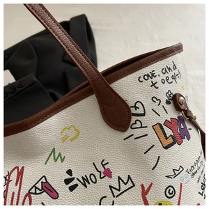 Close-up of a white tote bag featuring graffiti prints and pebbled leather texture