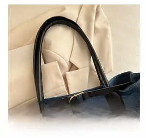 Dettaglio della borsa tote in denim blu con manico in pelle nera e fibbie in metallo dorato