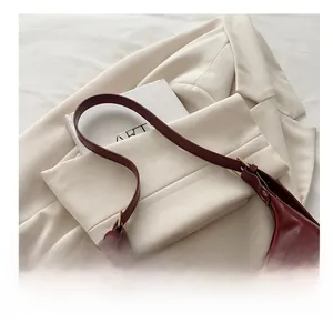 Close-up of wine red glossy leather baguette bag with gold hardware on a beige suit