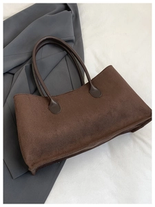 Flat lay of brown suede tote bag with dual handles on a minimalist white bedding background
