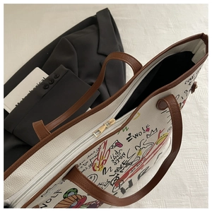 Detail of white tote bag with colorful graffiti art, brown leather handles and metal zipper