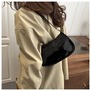 Detail of glossy black patent leather shoulder bag paired with a classic beige coat