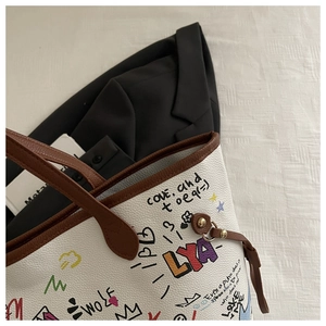 Close-up of white pebbled leather tote bag with colorful graffiti and brown trim handles